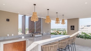 Una cocina exterior moderna con barra, que incluye una isla grande, taburetes de bar y lámparas colgantes.