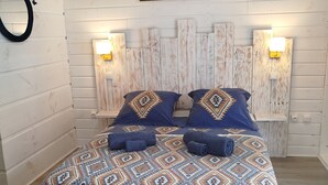 Un lit avec une couvre-lit à motifs, deux oreillers et une tête de lit agrémentée de lampes fixées au mur.