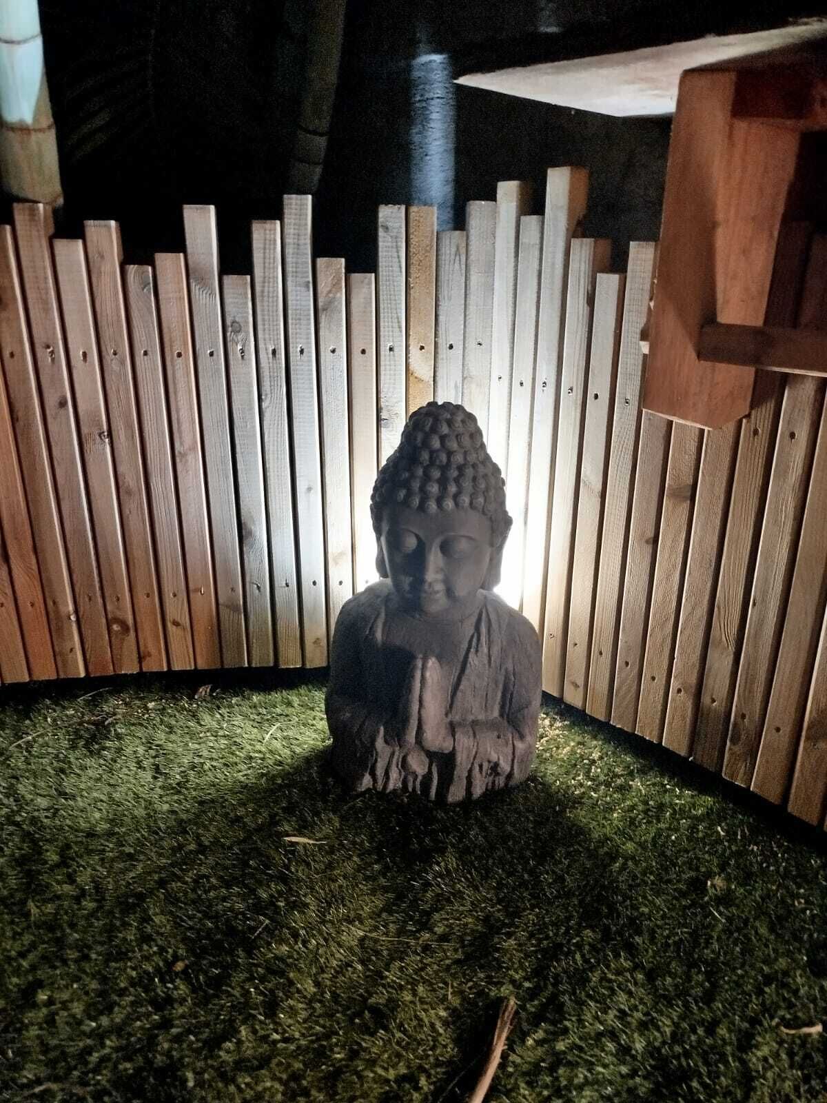 En Buddha-staty i ett hörn, med ett trästaket och ett fågelhus.