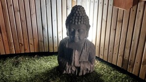 Une statue de Bouddha, placée dans un coin, avec une clôture en bois et une nichoir à oiseaux.