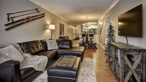 A modern living room with a leather sofa, a coffee table, and skis mounted on the wall. - The Eagles at Big White (Beaverdell)