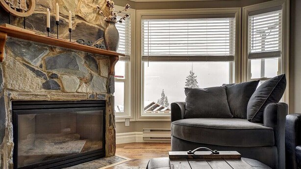 A cozy living room with a stone fireplace, a gray sofa, and a wooden coffee table. - The Eagles at Big White (Beaverdell)
