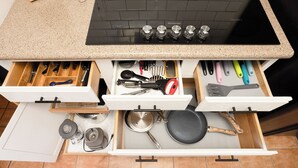 Een keuken met een zwart fornuis, een granieten aanrechtblad en meerdere lades met keukengerei en pannen.