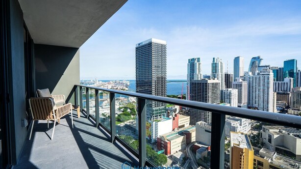 A balcony with a view of a city skyline, including a tall building with 'SKY' on it. - Apartment in New Luxury Condo Downtown (Miami)