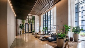A spacious lobby with a modern design, featuring a long corridor, large windows, and several seating areas with potted plants. - Apartment in New Luxury Condo Downtown (Miami)