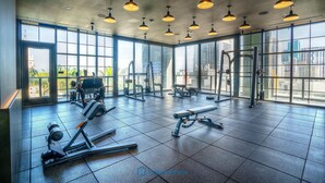 A spacious gym with large windows, various exercise equipment, and multiple hanging lights. - Apartment in New Luxury Condo Downtown (Miami)