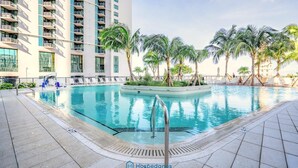 A swimming pool with a tiled deck, surrounded by palm trees and a high-rise building. - Apartment in New Luxury Condo Downtown (Miami)