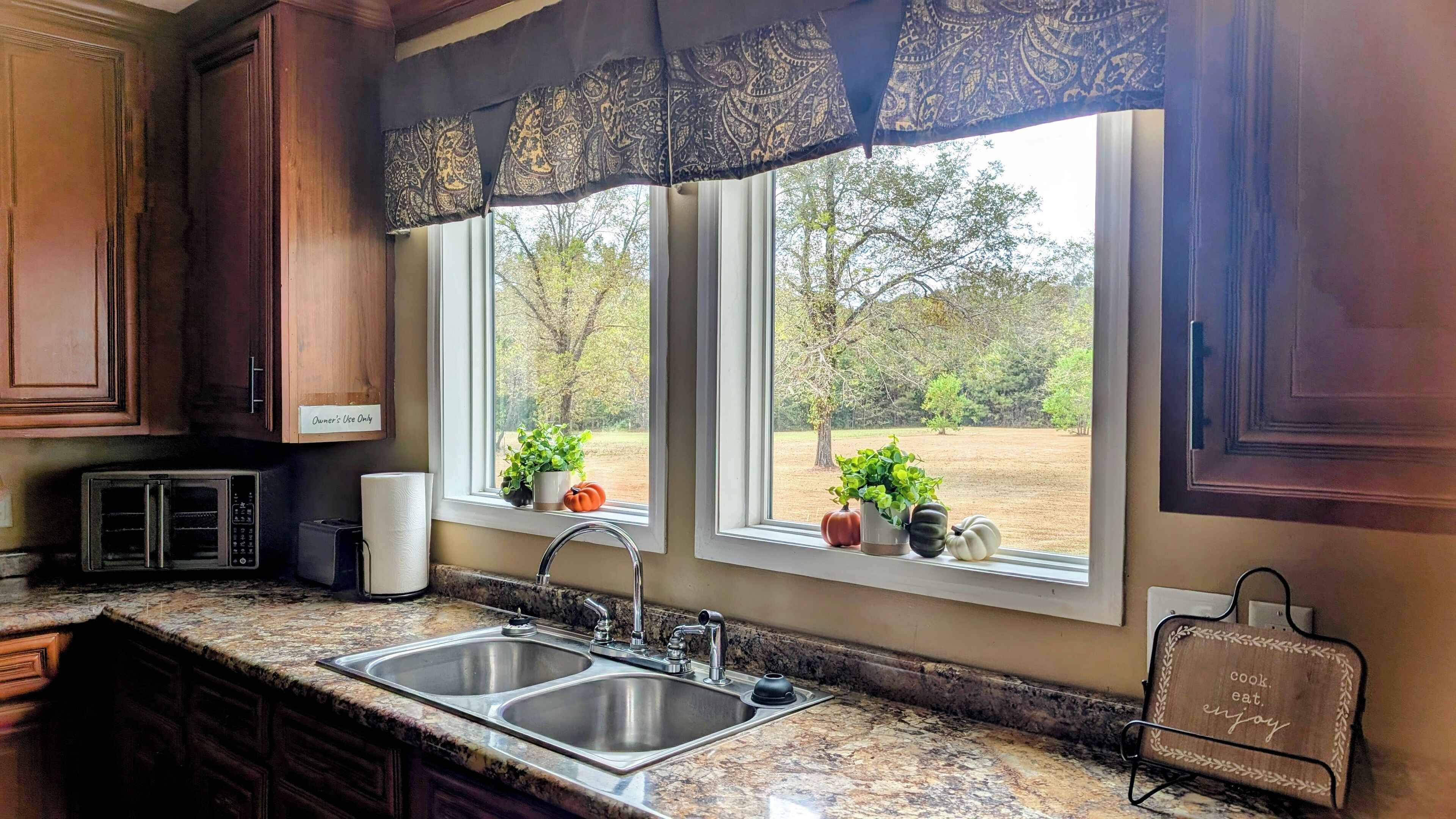 A kitchen with two sinks, a microwave, and a window with a view of trees.