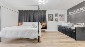 A modern bedroom with a four-poster bed, a dark sofa, and a wall with framed basketball jerseys. - Live the Game: Pool, Cinema, Gym, Jersey Wall (Massillon)