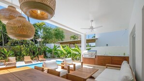Um pátio ao ar livre com piscina, móveis de madeira e luzes penduradas.