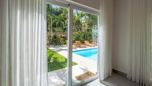 Quarto com porta de vidro deslizante que dá para área de piscina com espreguiçadeiras e palmeiras.