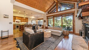 Amplia sala de estar con techo alto, vigas de madera, chimenea y ventanas grandes que ofrecen vistas al exterior.
