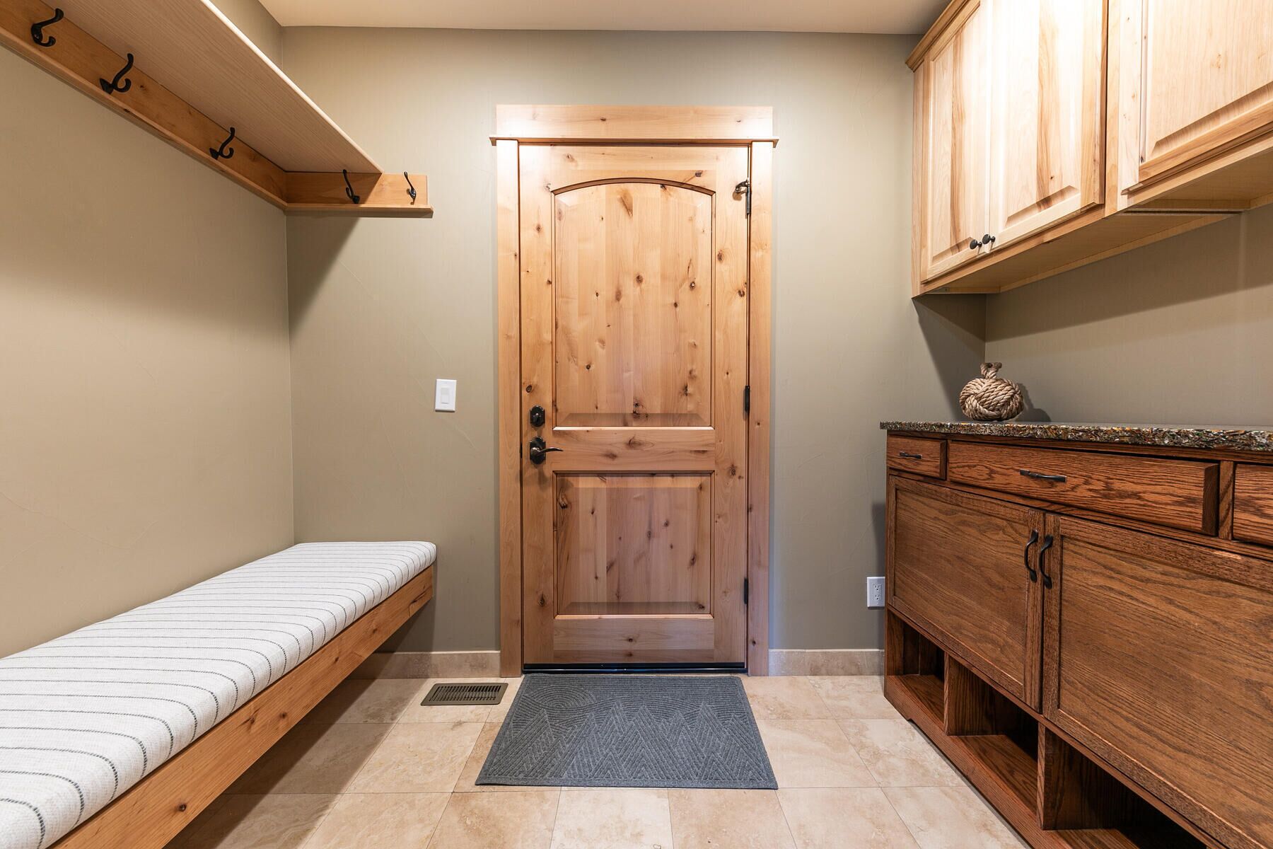 A small, cozy room with a wooden door, a bench, a cabinet, and a rug.