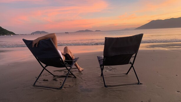 Dos sillas de playa mirando al océano con vistas al atardecer.