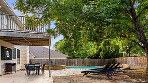A backyard with a stone patio, a pool, lounge chairs, and a dining area with a table and chairs.