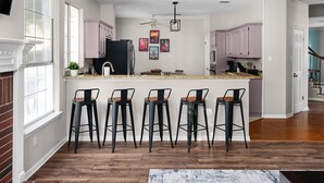 A modern kitchen with a central island, bar stools, and a ceiling fan.