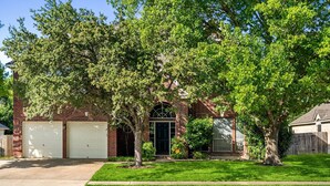 A two-story brick house with a garage, a front door, and a small front yard with a tree.