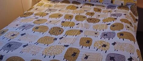 Una cama con colcha estampada que presenta diversos diseños de ovejas.