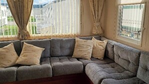 Un canapé d’angle gris avec des coussins à motifs, dans une pièce dotée de grandes fenêtres et de rideaux.