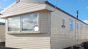 Une maison mobile dotée d’une grande fenêtre, d’une cheminée et d’une antenne parabolique.