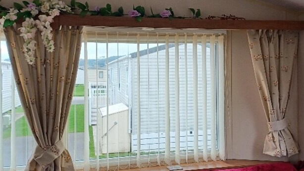 Une pièce dotée d’une grande fenêtre avec des stores blancs, un cadre de fenêtre en bois et donnant sur un quartier résidentiel.