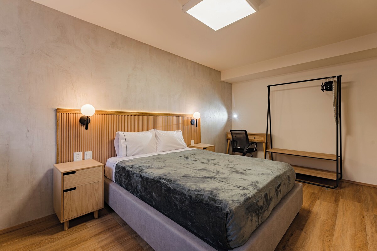 A modern bedroom with a bed, bedside tables, a desk, and a large mirror.