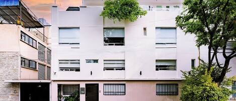 A multi-story building with a flat facade, a balcony, and a small garden area.