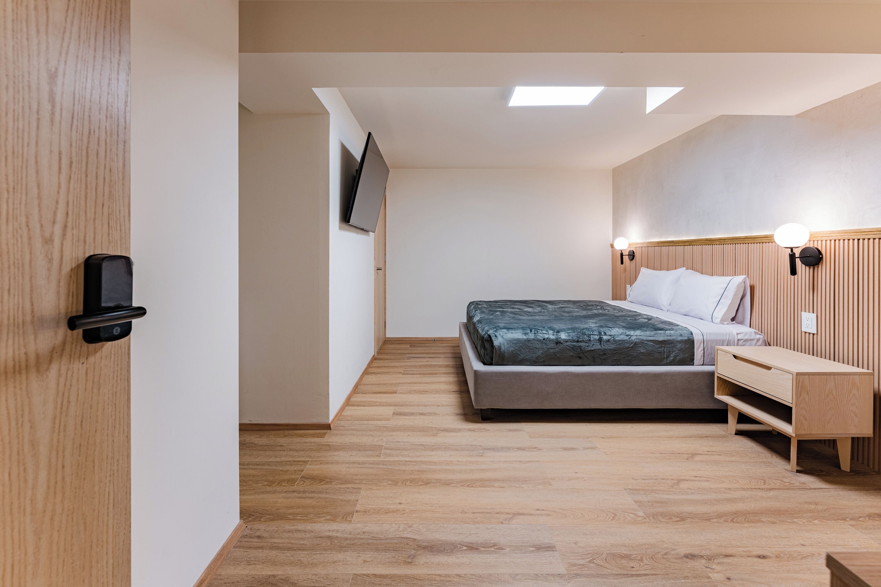 A bedroom with a bed, bedside table, wall-mounted TV, and a wooden headboard.