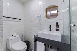A modern bathroom with white tiles, a white toilet, a black sink, a mirror, and a handheld hair dryer. - Escandon Suites by Escajal Room (Mexico City)