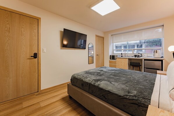 A bedroom with a bed, a desk, a chair, a television, and a window with blinds. - Escandon Suites by Escajal Room (Mexico City)