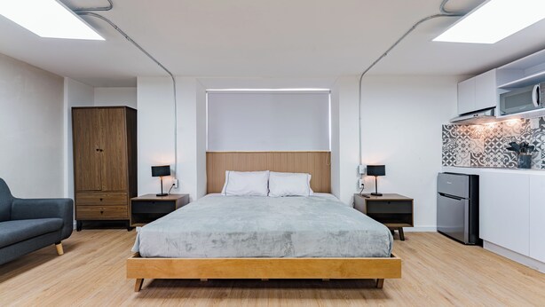 A modern bedroom with a wooden bed, bedside tables, a wardrobe, and a kitchenette. - Escandon Suites by Escajal Room (Mexico City)