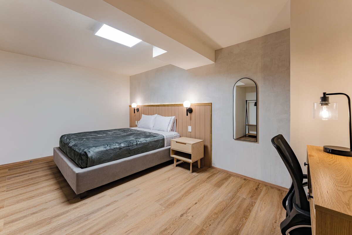 Een moderne slaapkamer met een bed, nachtkastje, stoel en een spiegel aan de muur.