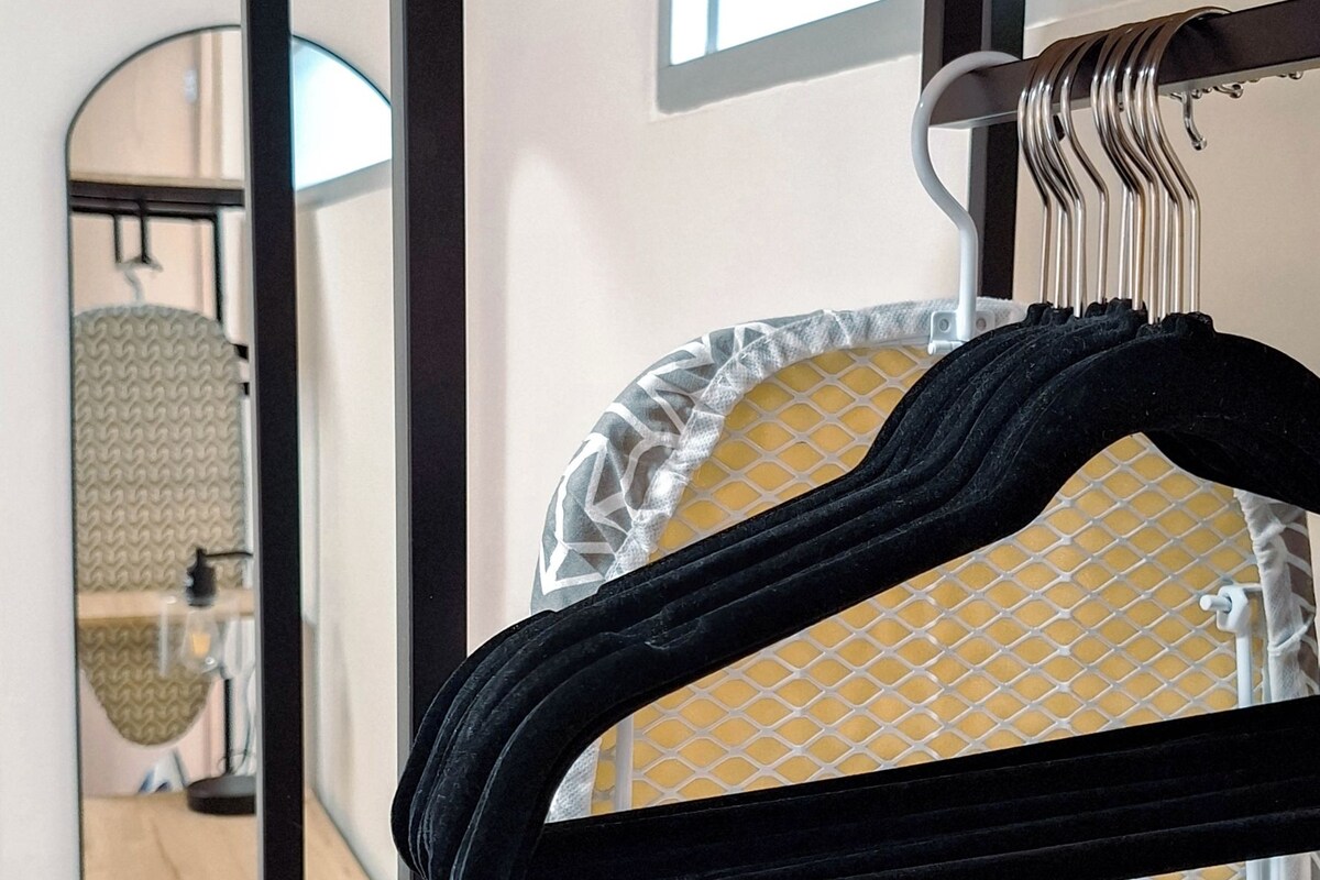 Een kamer met een metalen strijkplank, een spiegel en een houten plank.
