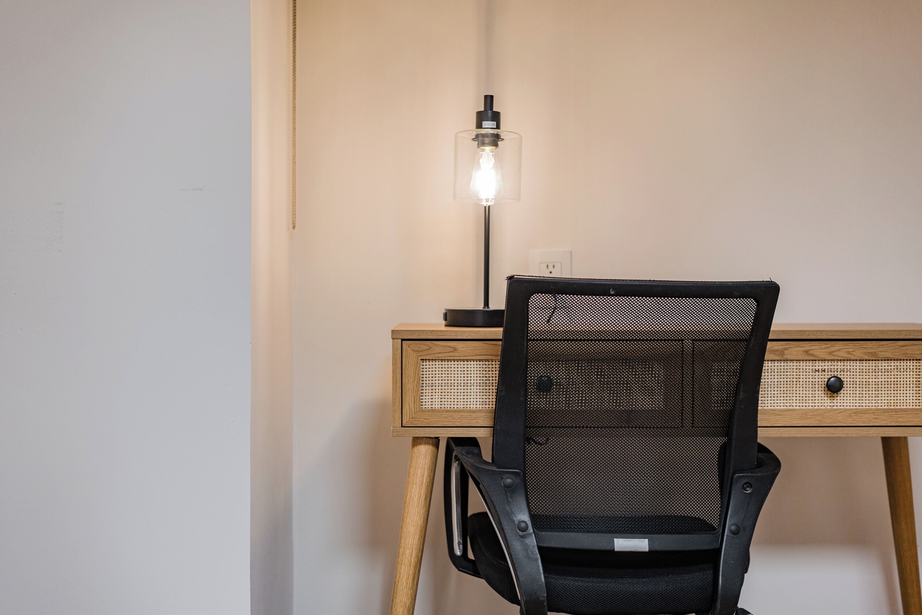 Un escritorio de madera con una silla de malla, una lámpara y un enchufe.