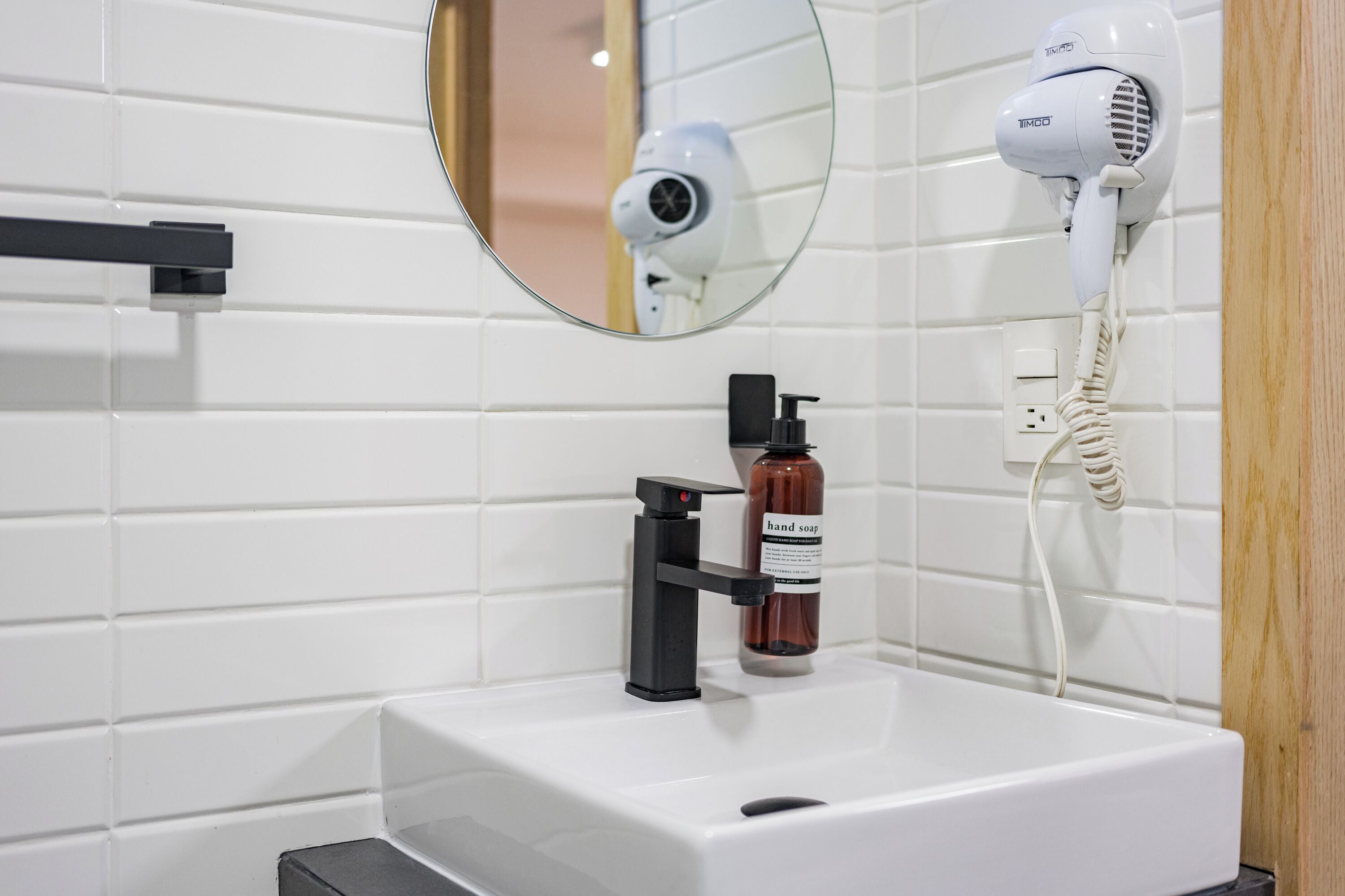 A bathroom with a white sink, a mirror, a hairdryer, and a bottle of hand soap.