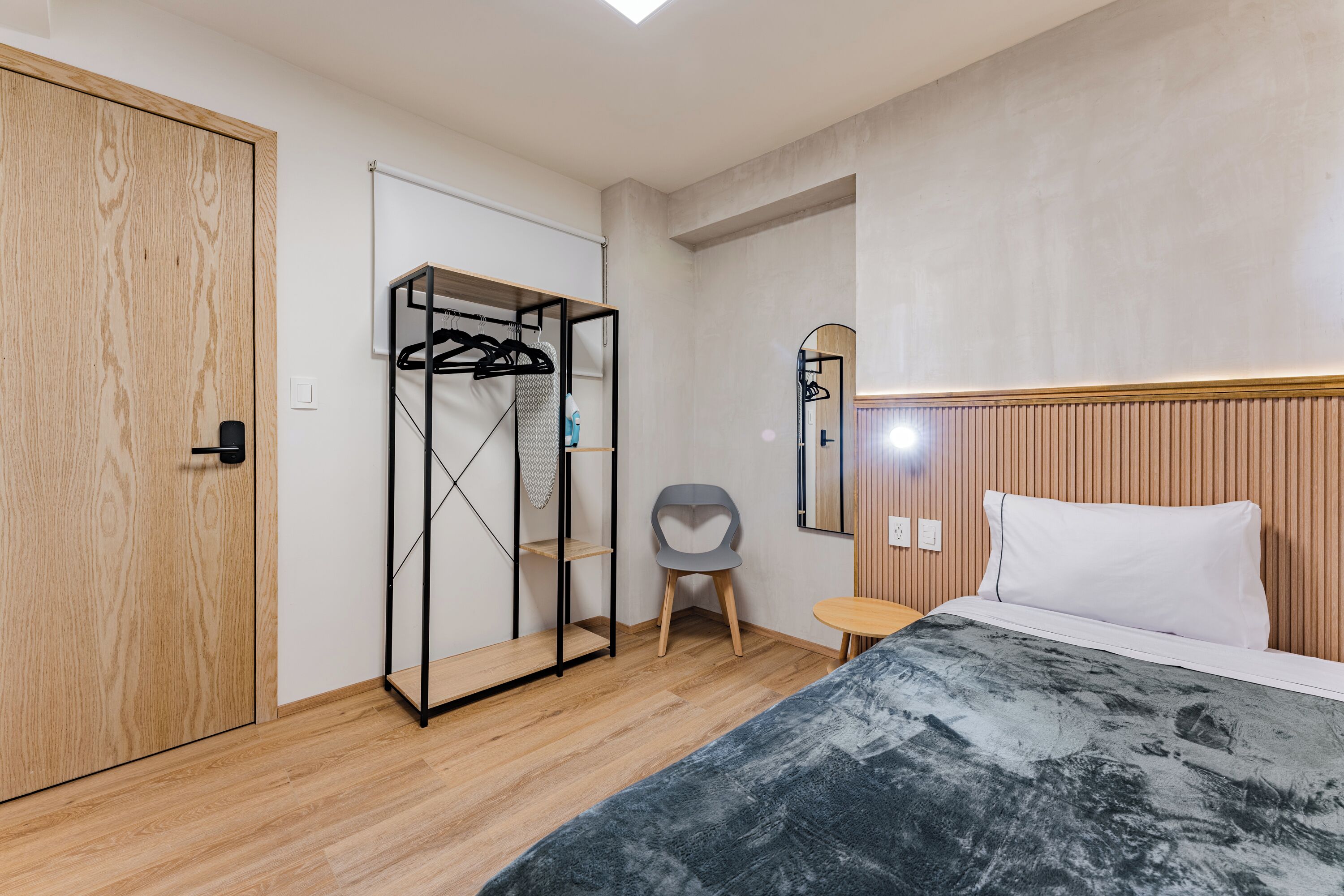 A bedroom with a wooden wardrobe, a bed with a white pillow, a small table, and a chair.