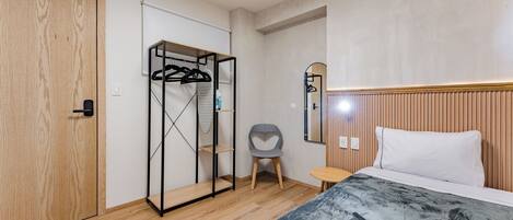A bedroom with a wooden wardrobe, a bed with a white pillow, a small table, and a chair.