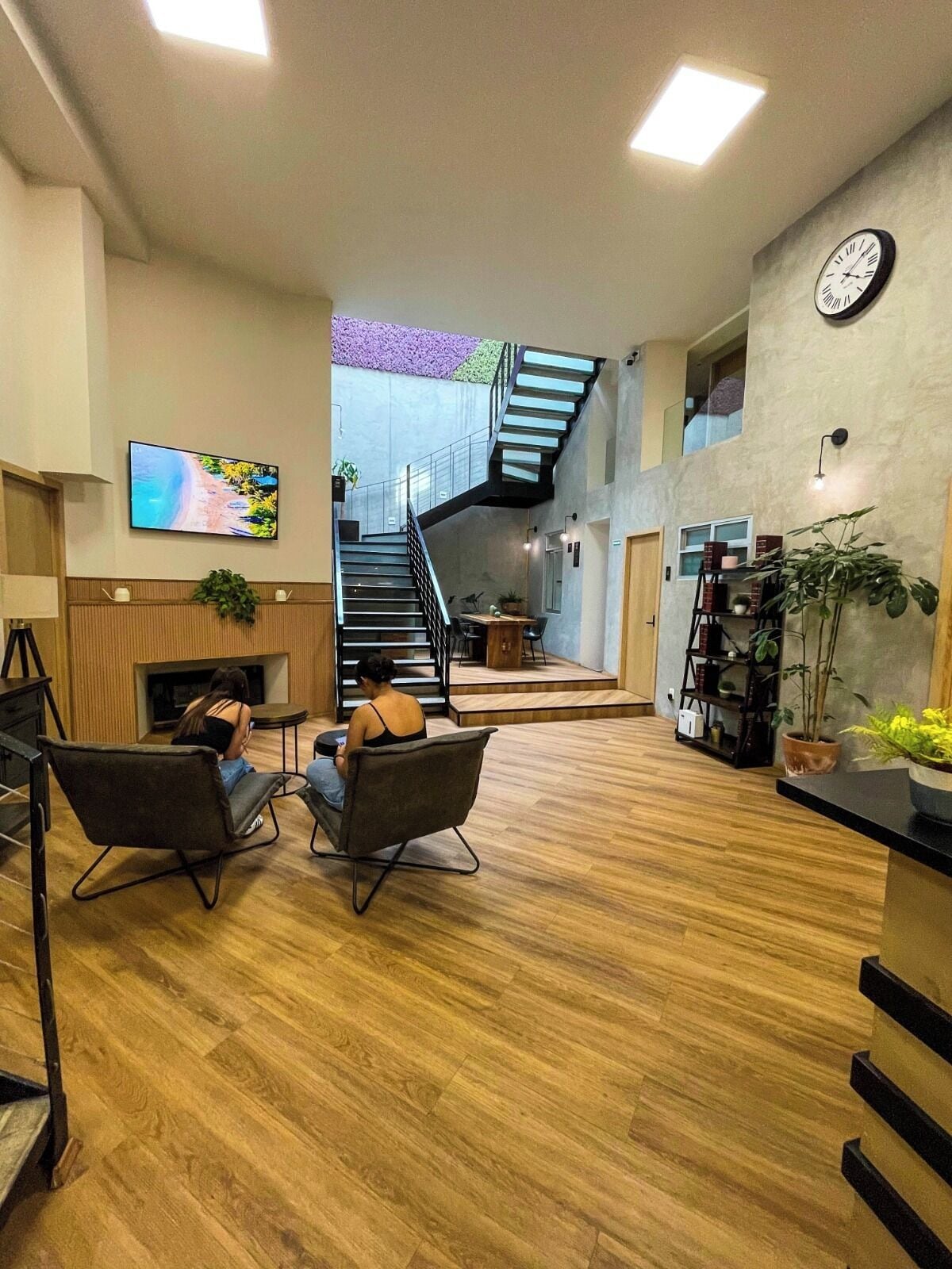 Eine geräumige Lobby mit Holzboden, einer Treppe, einem Flachbildfernseher und einer Wanduhr.