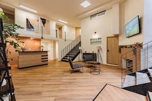 Experience the stylish reception area with a comfortable seating area, wooden counter, and a large wall-mounted TV.