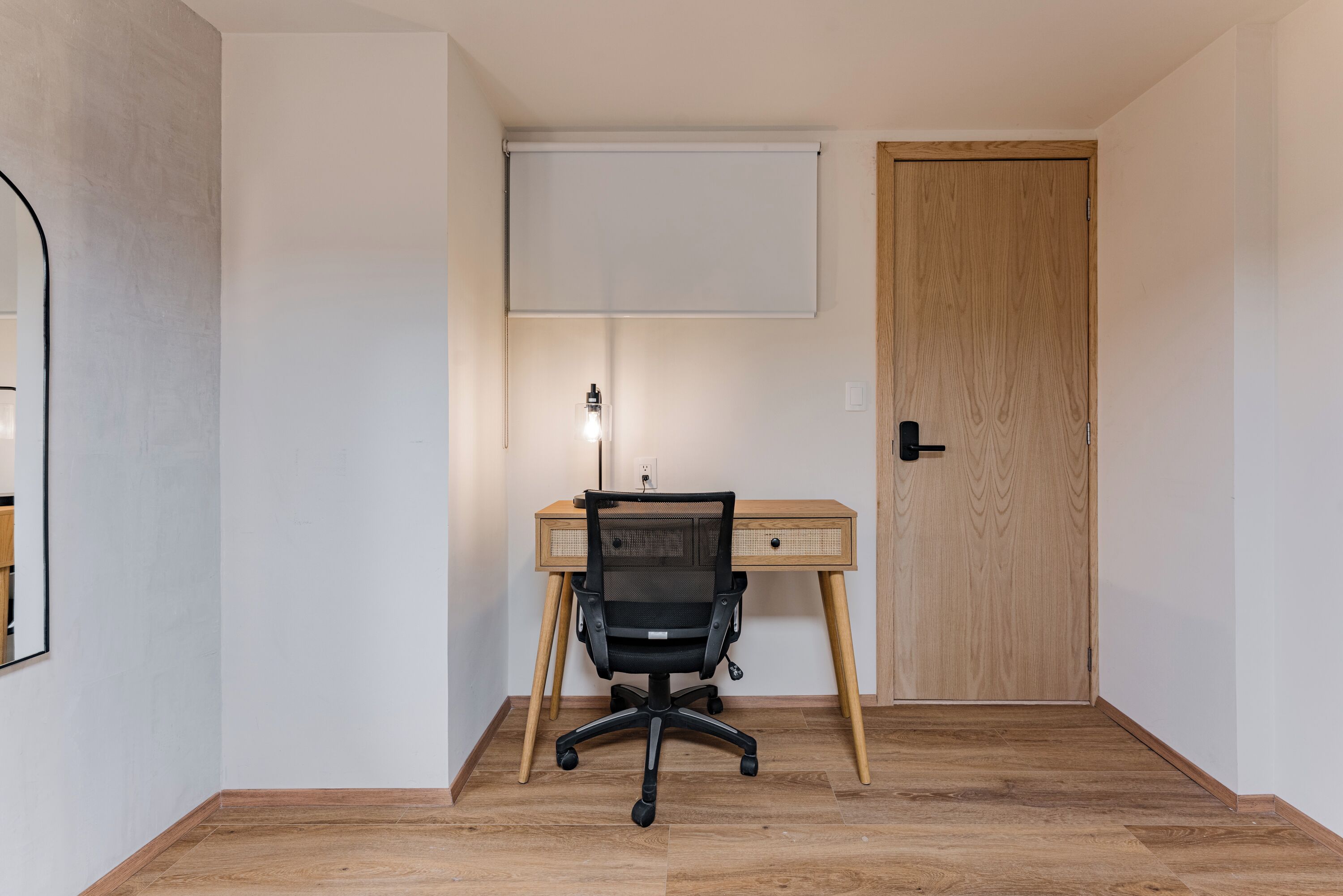A room with a wooden desk, a black office chair, a whiteboard, and a door.