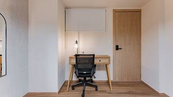 A room with a wooden desk, a black office chair, a whiteboard, and a door.