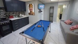 A living room with a pool table, a television, and a kitchen area.