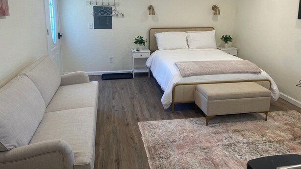 A bedroom with a bed, bedside tables, a nightstand, a sofa, a bench, and a rug.