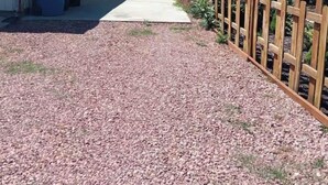 A residential area with a gravel driveway, a wooden fence, and a pathway leading to a house.