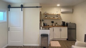 A compact kitchen with white cabinets, a stainless steel refrigerator, and a black trash bin.