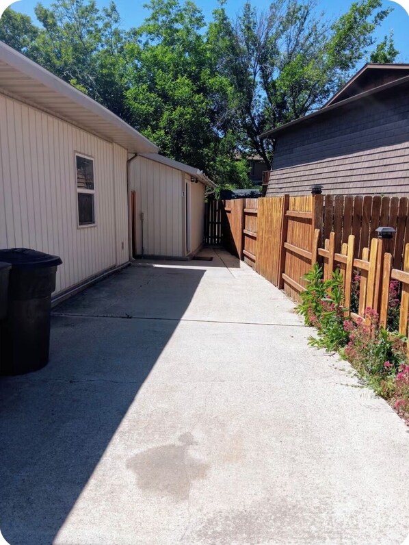 A residential backyard with a concrete pathway leading to a wooden gate, surrounded by a wooden fence and a shed. - Chic studio hideaway in Riverdale with AC, Wifi (Riverdale)