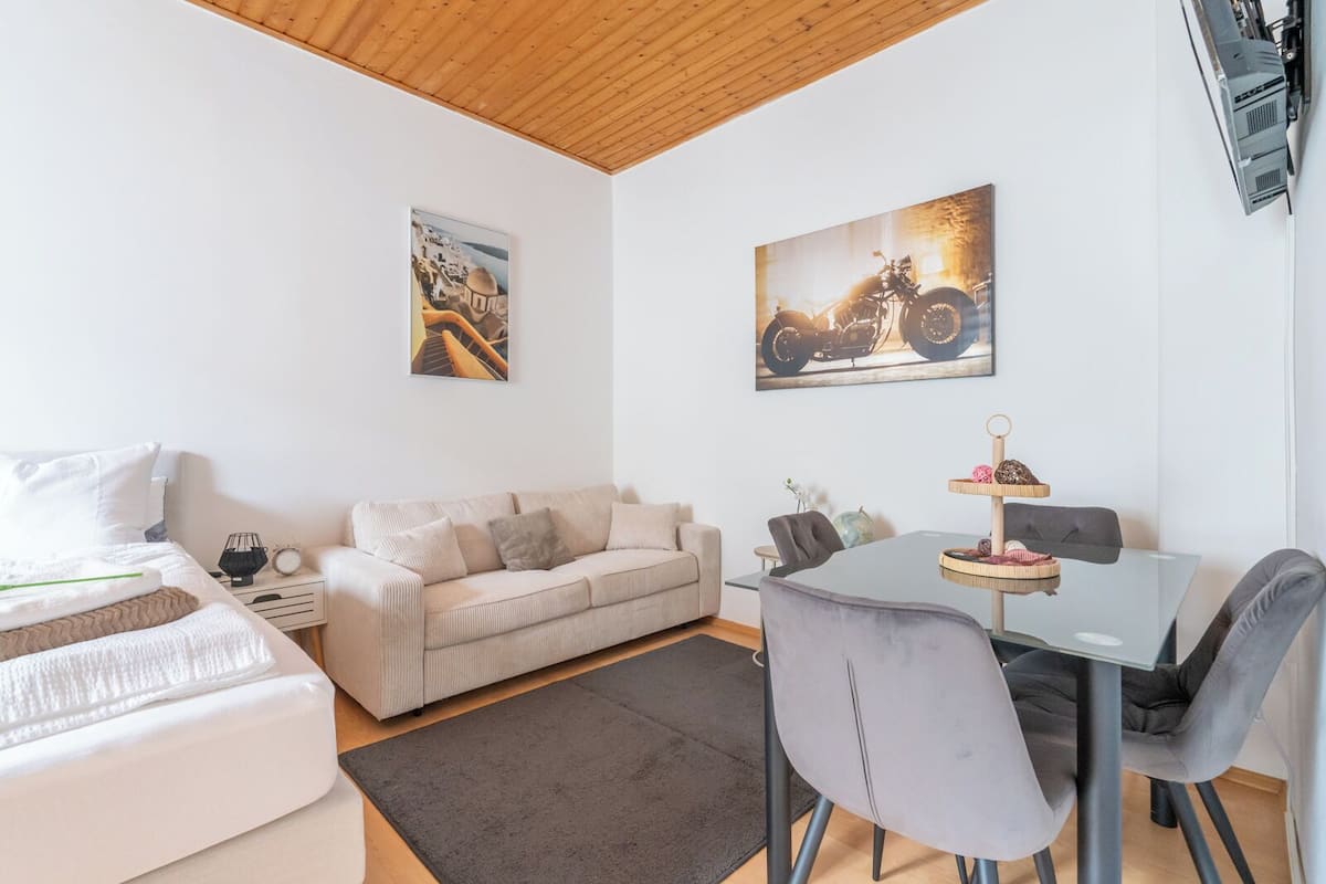 A modern living room with a sofa, a dining table with chairs, and two wall-mounted artworks.