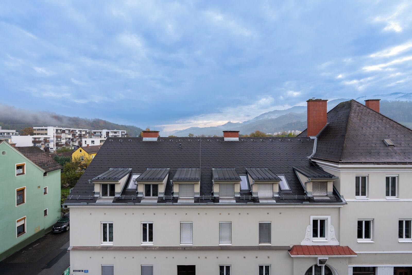 Une rangée d’immeubles résidentiels à plusieurs niveaux, dont certains sont dotés de lucarnes, se dressant sur fond de montagnes et d’un ciel nuageux.