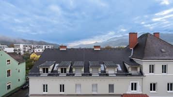 Une rangée d’immeubles résidentiels à plusieurs niveaux, dont certains sont dotés de lucarnes, se dressant sur fond de montagnes et d’un ciel nuageux.