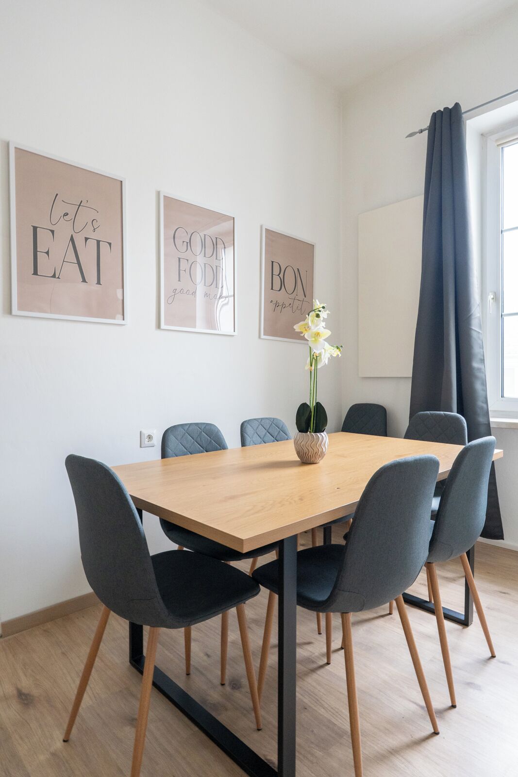 Een eetruimte met een houten tafel, zes grijze stoelen en drie motiverende posters in lijsten aan de muur.